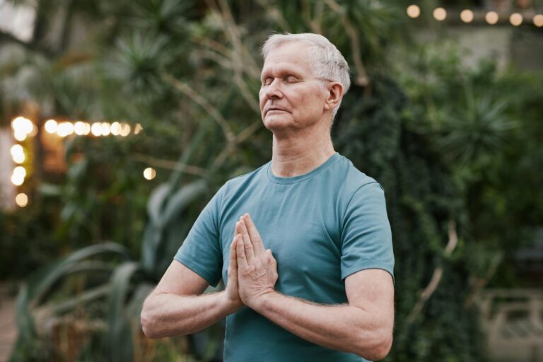 Serene elderly man meditating outdoors in a tranquil garden setting, focusing on peace and mindfulness.